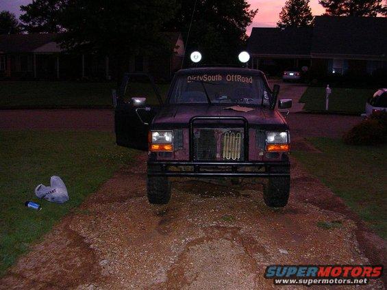 Dark purple 1989 Ford Bronco II with aftermarket grille guard and off-road lights, parked on a gravel driveway