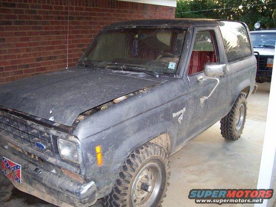 Dark gray Ford Bronco II with red interior, hood open, parked next to another SUV