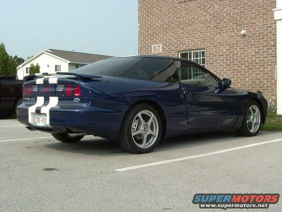 Blue 1995 Ford Probe parked in a lot, showing rear quarter panel and racing stripes on the trunk lid