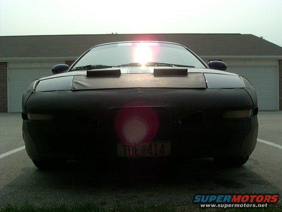 Car front covered in black fabric, headlights visible, license plate TDE-414