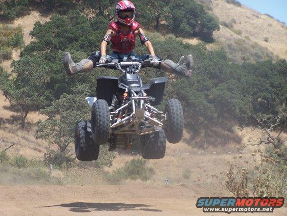 Person in full gear jumps an ATV mid-air with legs spread wide