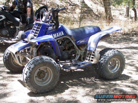 Blue 2001 Yamaha BANSHEE ATV with knobby tires, parked on dirt. A person on another ATV is visible to the left