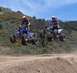 2001 Yamaha BANSHEE - Two ATVs jump a dirt track with riders in helmets.