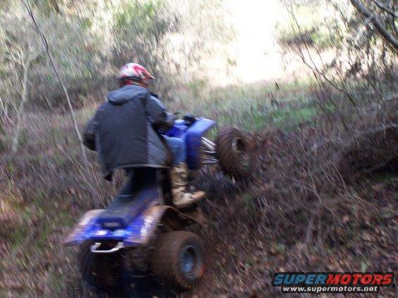 Rider on blue ATV going up a muddy hill in woods