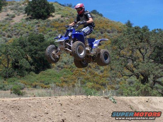 Blue 2001 Yamaha BANSHEE ATV mid-air jump, rider wearing red helmet and protective gear