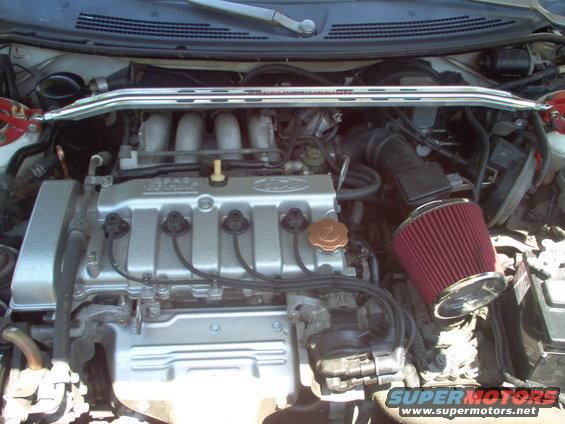 Engine bay of a car, showing the Ford engine, intake manifold, and a red aftermarket air filter. A strut bar is visible across the top