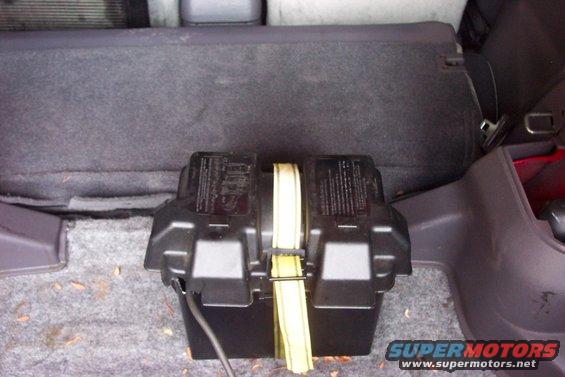 Car trunk with a black battery box secured by a yellow strap