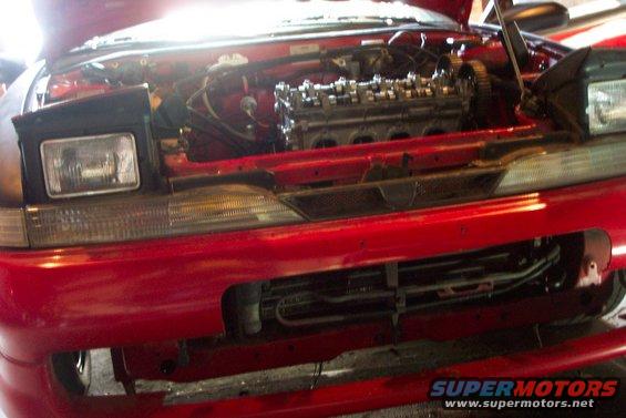 red car front end with hood open showing engine and parts of the front bumper and headlights