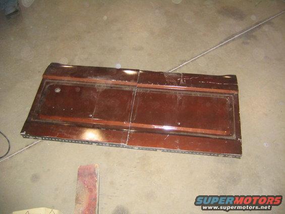 Brown car door panel with woodgrain trim and a circular cutout, lying flat on a concrete floor