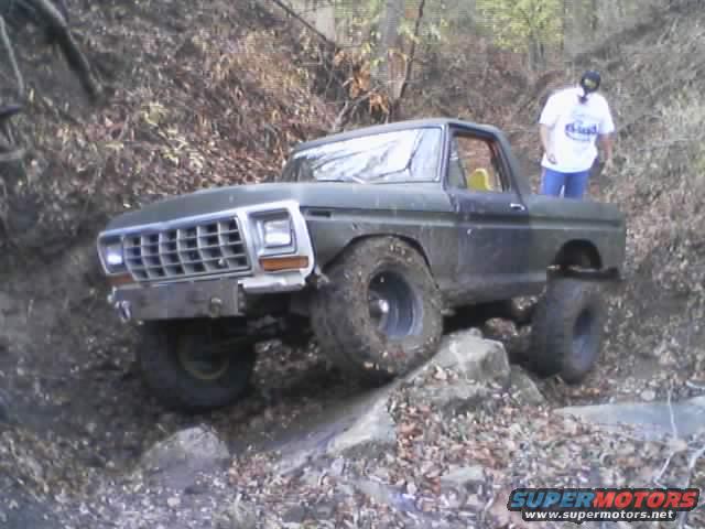 Green 1978 Ford Bronco with large tires navigating rocky terrain, person standing nearby