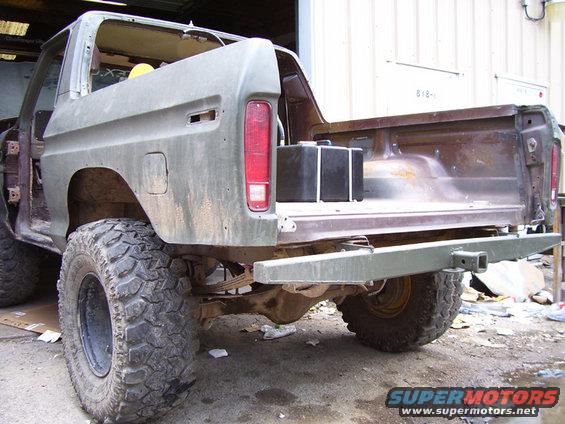 Rear 3/4 view of a 1979 Ford Bronco in olive green, missing doors and roof, with large off-road tires