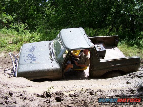 Olive green pickup truck stuck in mud with a man driving