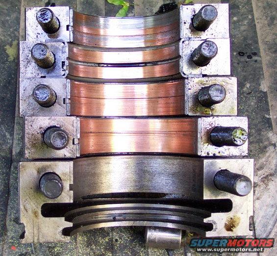 Engine bearing caps with copper inserts and a crankshaft pulley. The caps are bolted to metal blocks