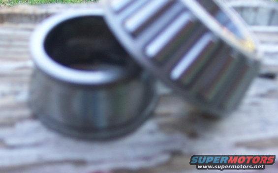 Two metal bearings, one with visible roller cage, resting on a wooden surface