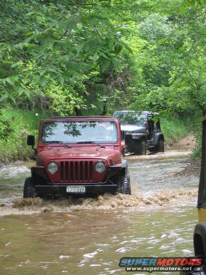 1998 Jeep TJ and another Jeep driving through a muddy creek, front view of red Jeep