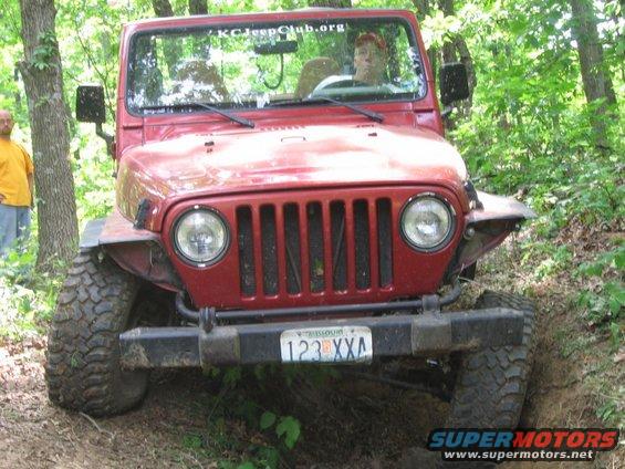 Front view of a red 1998 Jeep TJ on a wooded trail, driver visible