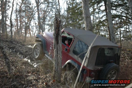 Red 1998 Jeep TJ off-roading through mud and trees