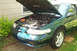 1995 Ford Taurus - The engine bay of a green sedan is exposed, with the hood propped open. The car appears to be a 1995 Ford Taurus SHO.