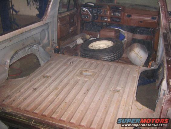 Interior of a vehicle with the rear cargo area stripped down and the spare tire visible in the passenger area