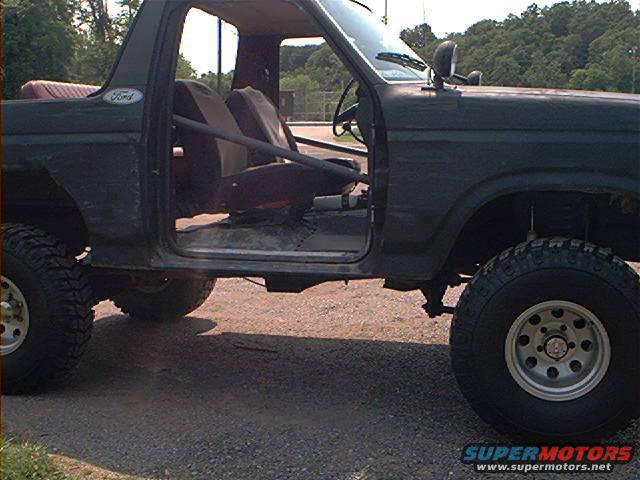 Side view of a dark 1986 Ford Bronco with doors removed and roll cage