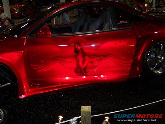 Red car with custom airbrush art of a winged figure on the side door. Aftermarket wheels visible
