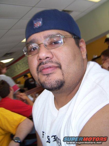 Man wearing glasses and a blue NFL cap, with text on shirt and Supermotors.net logo