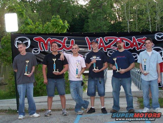 Six men stand in front of a banner that says "MXU MAZDAS". They are holding trophies