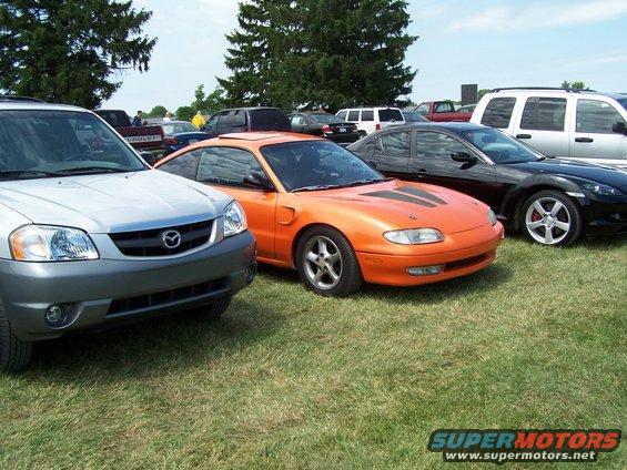 Orange Mazda MX-6 coupe with black hood stripes, parked on grass