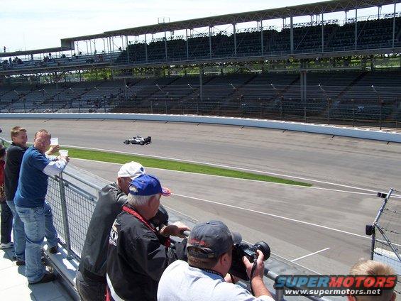 Race car on track with spectators in foreground, grandstands in background