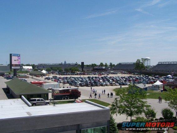 Parking lot filled with cars under a clear blue sky, with a stadium and water tower in the background