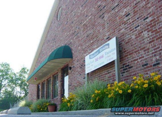 Brick building with green awning and a sign that says "Shelter Hours"