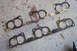 1995 Ford Taurus - Four exhaust manifold gaskets are laid out on a speckled concrete floor.