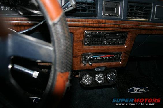 Dashboard of a 1989 Ford Crown Victoria LTD with wood grain trim, aftermarket gauges, and a Ford floor mat