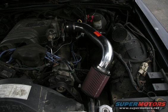 Engine bay with shiny intake tube and red air filter. Some wiring and engine parts visible