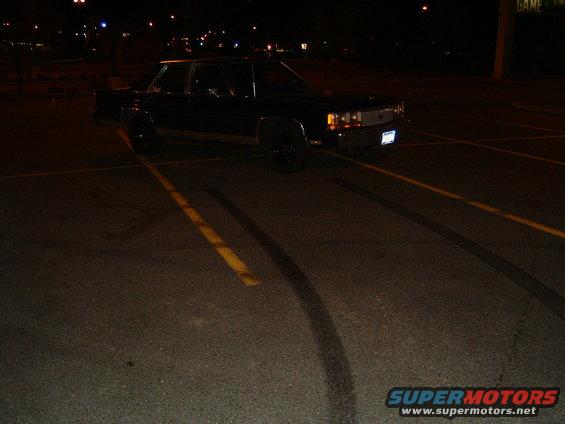 Black Ford Crown Victoria parked at night with tire marks on the asphalt