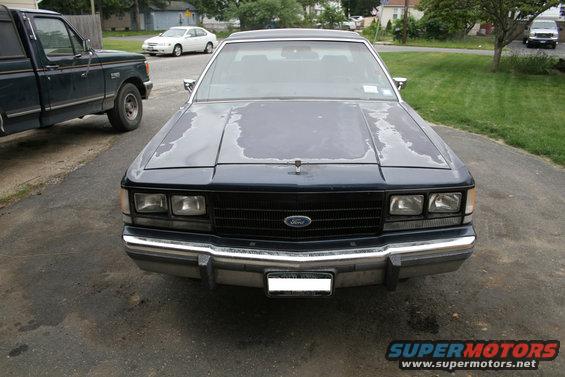 Dark blue Ford Crown Victoria with peeling paint on hood, front view