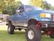 1988 Ford Pickup - A lifted blue pickup truck with a "FOR SALE" sign is parked on a grassy lawn.