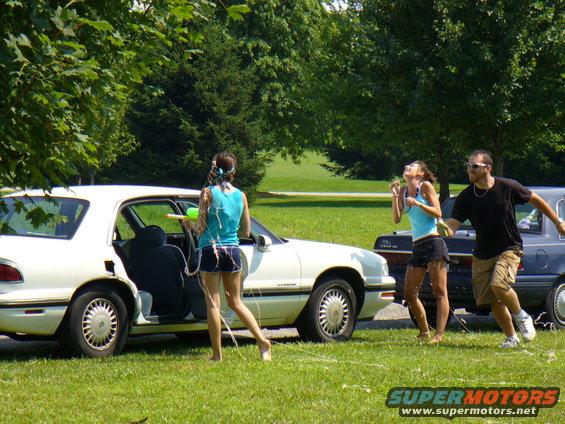 People with water guns by a white sedan and a dark car