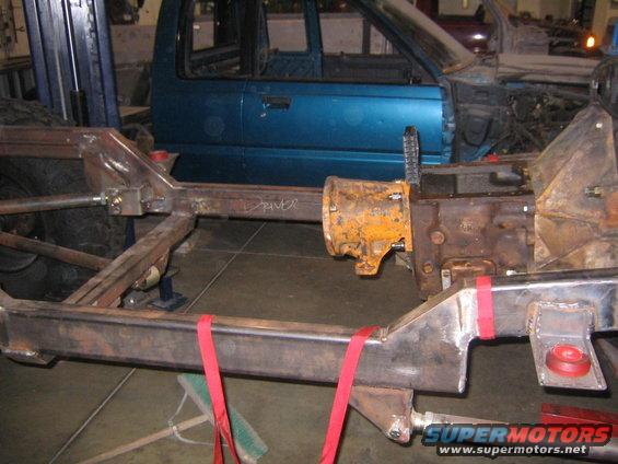 close-up of vehicle frame with transmission and transfer case, blue truck cab in background