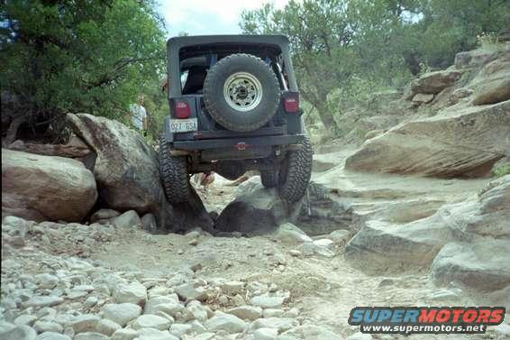 Black Jeep Wrangler on rocky terrain, rear view, spare tire mounted on back