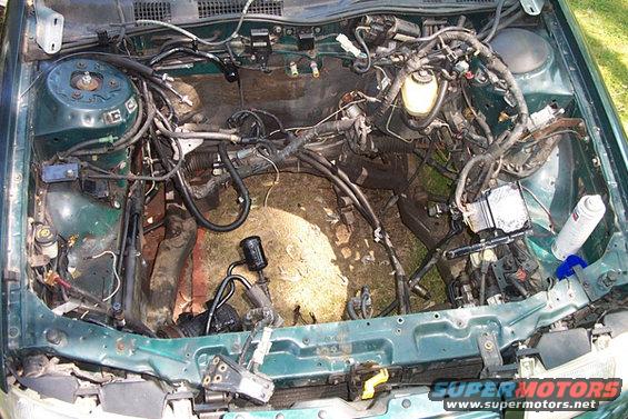 Green 1995 Ford Taurus engine bay with engine removed, showing wiring and components