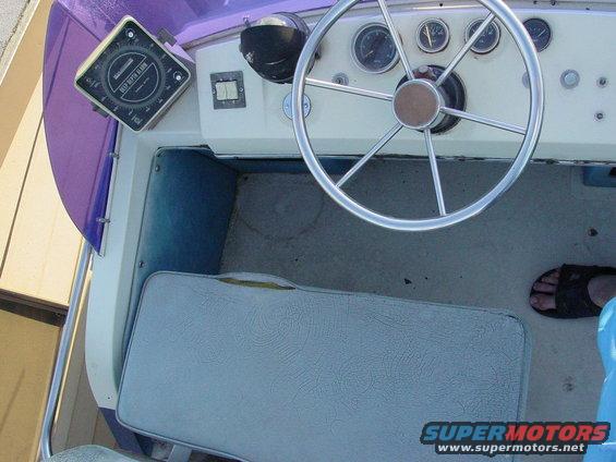 Boat interior with a compass, steering wheel, and gauges. Light blue seats are visible