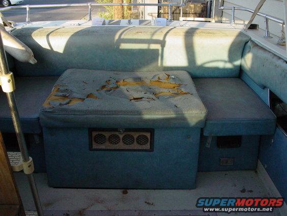 Boat interior with torn blue cushions and a central storage unit with vents