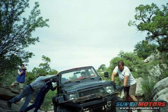 Black off-road vehicle with people pushing it on a rocky trail