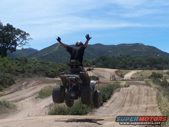 Person on a quad bike airborne over a dirt track with hills in background