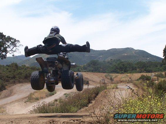ATV rider mid-air doing a split, with mountains in background