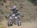 1999 Yamaha WARRIOR - A rider performs a jump on a four-wheeler, with the vehicle suspended in the air against a grassy hillside.