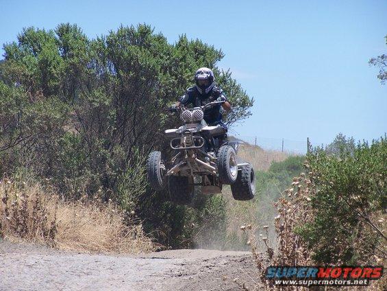 Quad bike rider airborne over a dirt track with trees and bushes