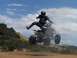1999 Yamaha WARRIOR - A rider soars through the air on a quad bike against a backdrop of hills and clouds.