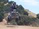 1999 Yamaha WARRIOR - A quad bike rider performs a jump with feet up in the air against a backdrop of hills and trees.